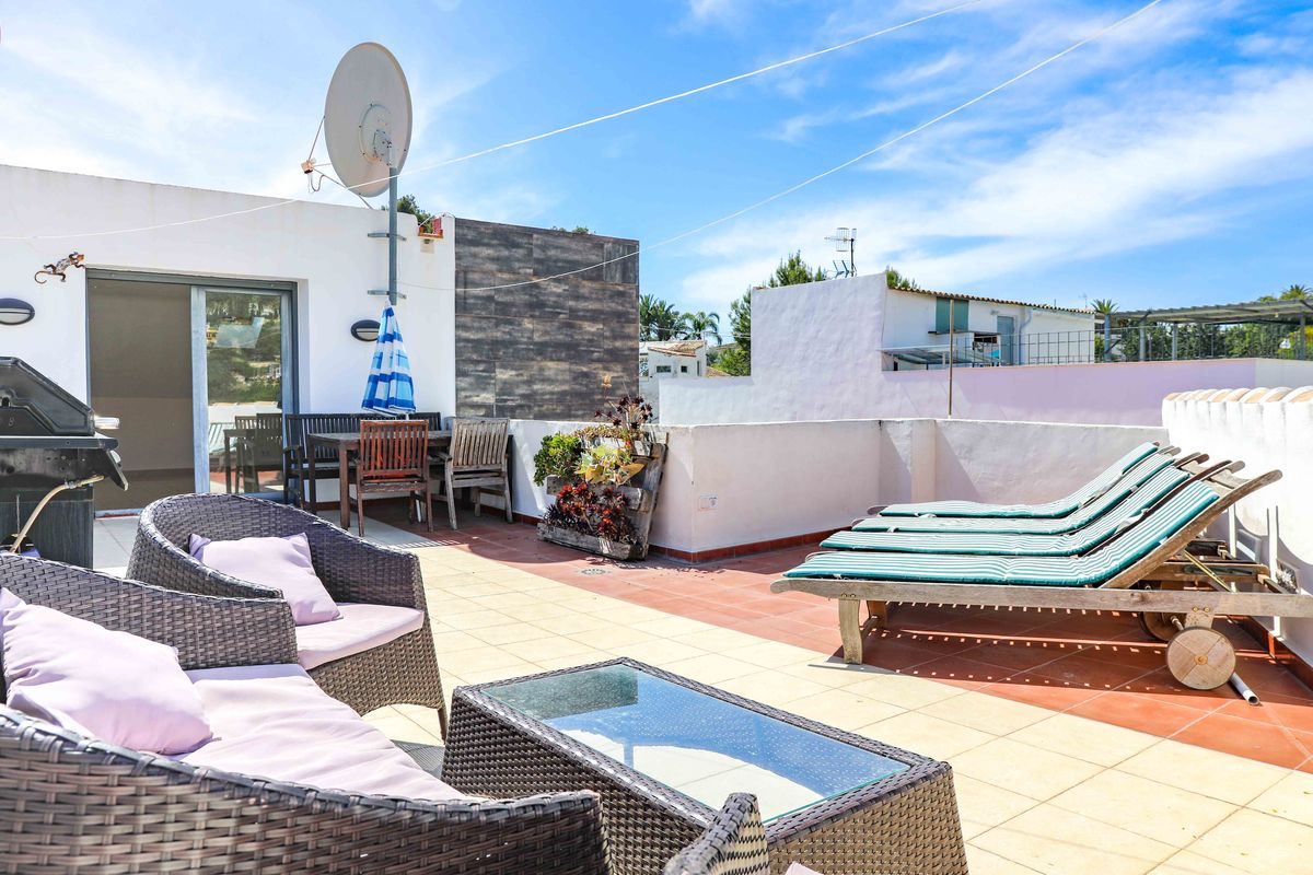Terrasse de toit avec salon en rotin, transats en bois et espace dînatoire. Comprend un sol carrelé, un barbecue et une antenne satellite sous un ciel dégagé.