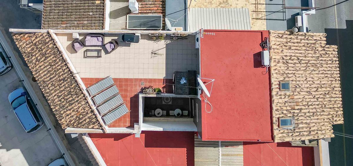 Vue aérienne d'un toit-terrasse à plusieurs niveaux comprenant un espace salon extérieur, des panneaux solaires et un mélange de tuiles traditionnelles et de surfaces planes.