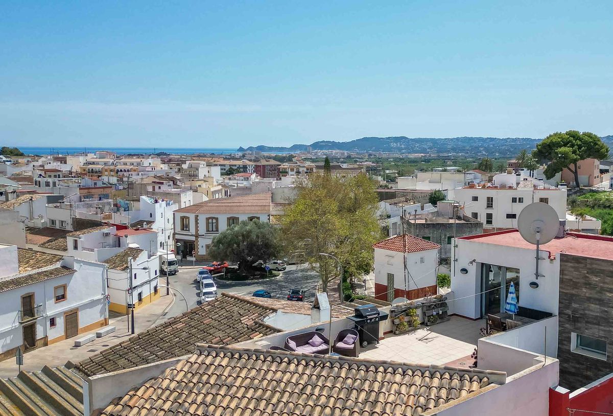 Vue surélevée d'un village méditerranéen avec une terrasse privée aménagée d'un barbecue, offrant un panorama sur les toits blancs et la mer.