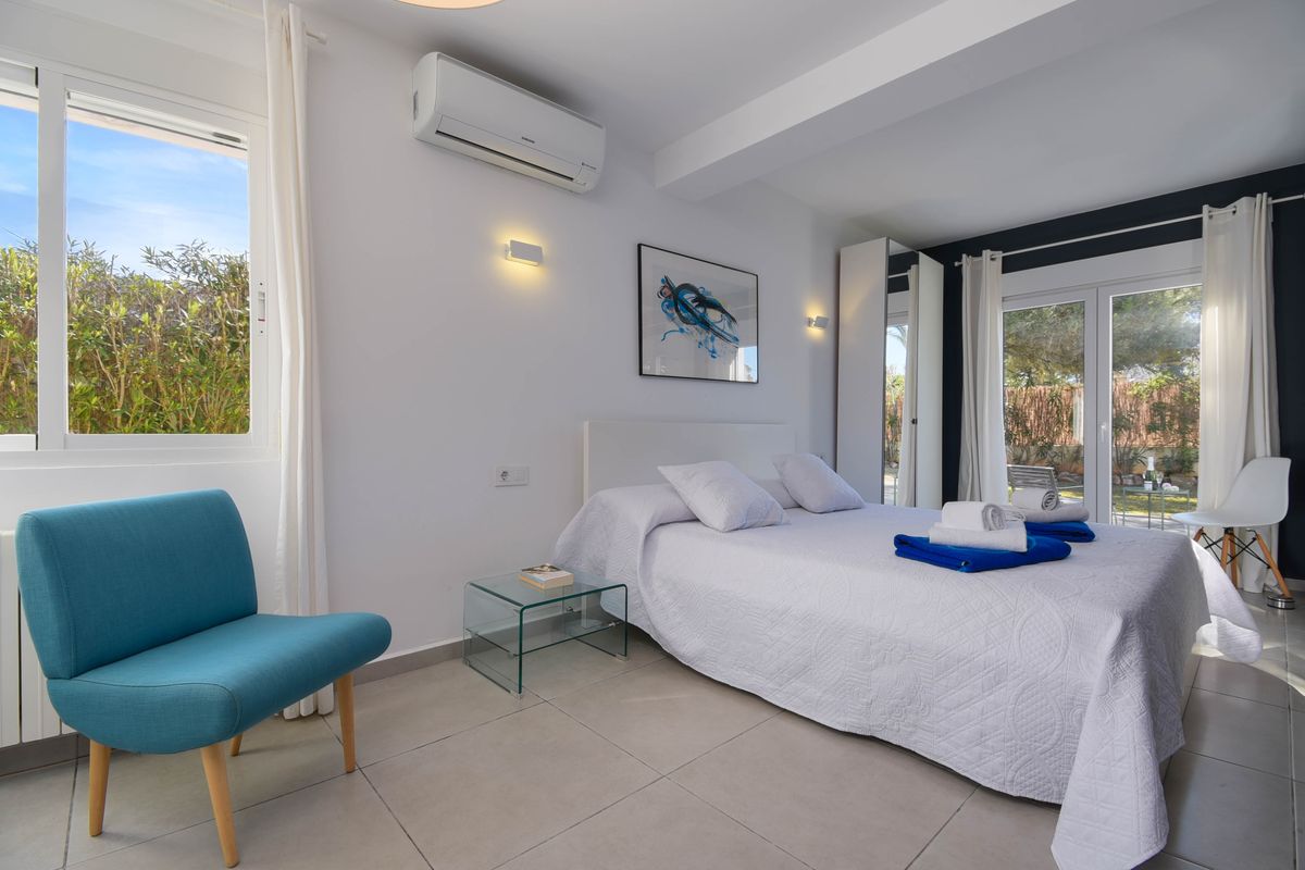 Chambre lumineuse avec lit double, fauteuil turquoise et table de chevet en verre. Équipée de la climatisation et d'un accès direct au jardin par baie vitrée.