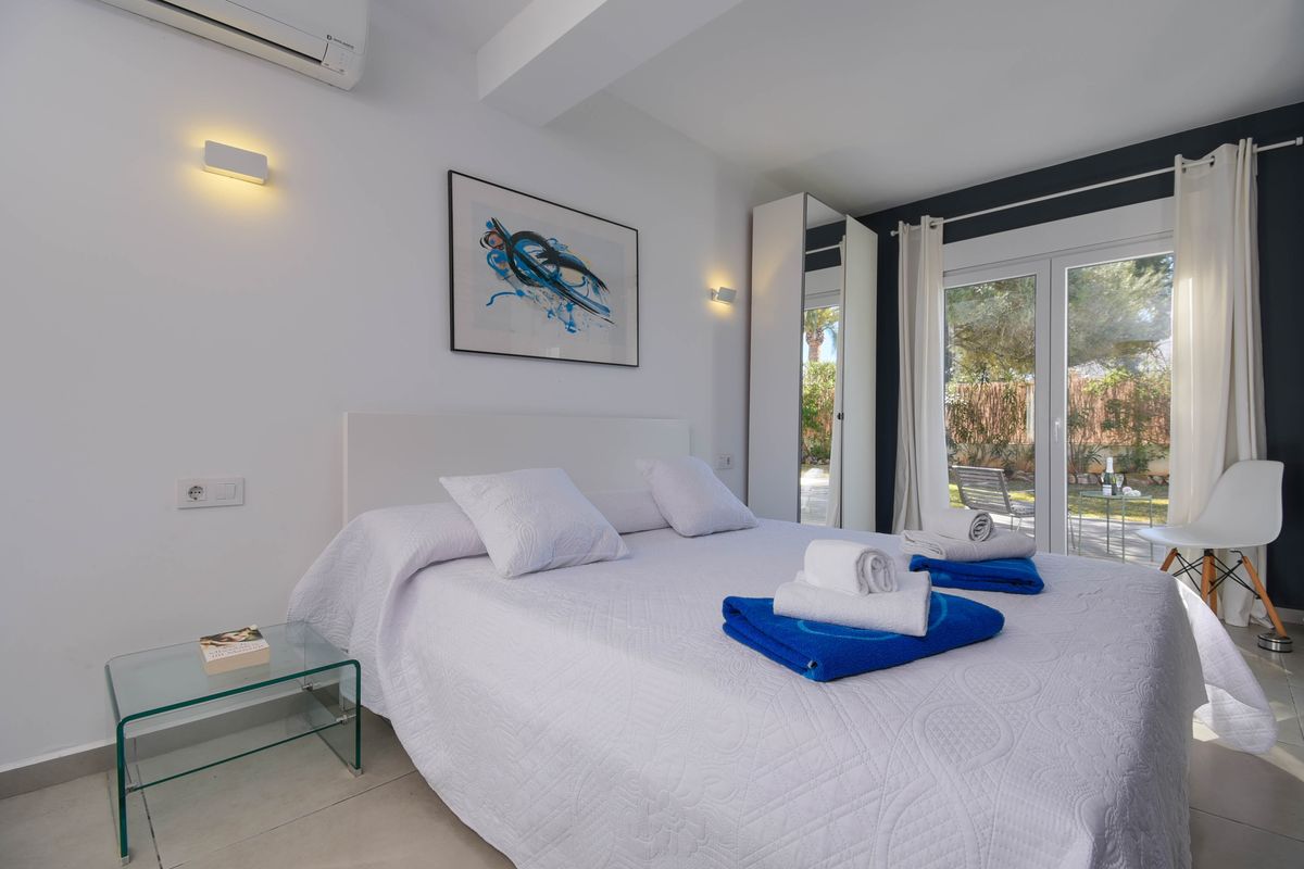 Chambre moderne avec lit double, table de chevet en verre et accès direct au jardin. La pièce dispose d'un mur d'accent sombre et de grandes baies vitrées lumineuses.