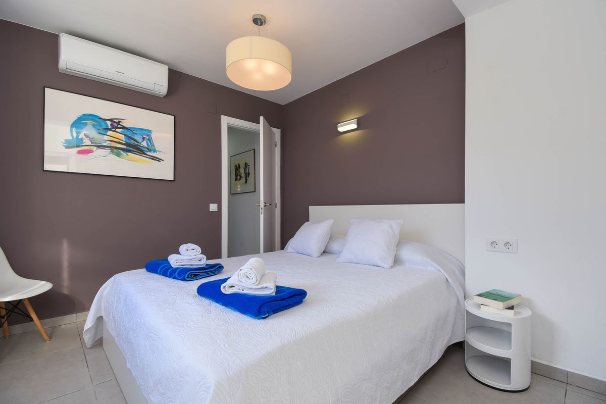 Chambre moderne avec mur d'accent mauve, art abstrait et lit double. Équipée de la climatisation et d'une table de chevet circulaire minimaliste.