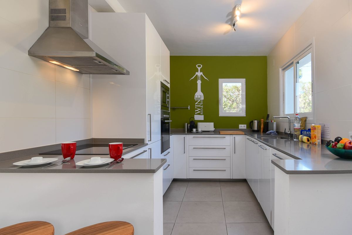 Cuisine moderne en U avec meubles blancs brillants, plans de travail en pierre grise, mur d'accent vert olive et électroménager intégré en inox.