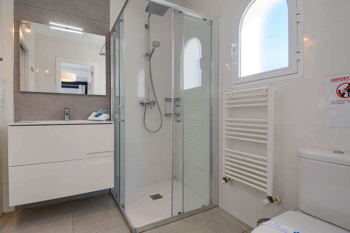 Salle de bain moderne avec cabine de douche en verre, meuble vasque blanc, radiateur sèche-serviettes et fenêtre en arc apportant une lumière naturelle.