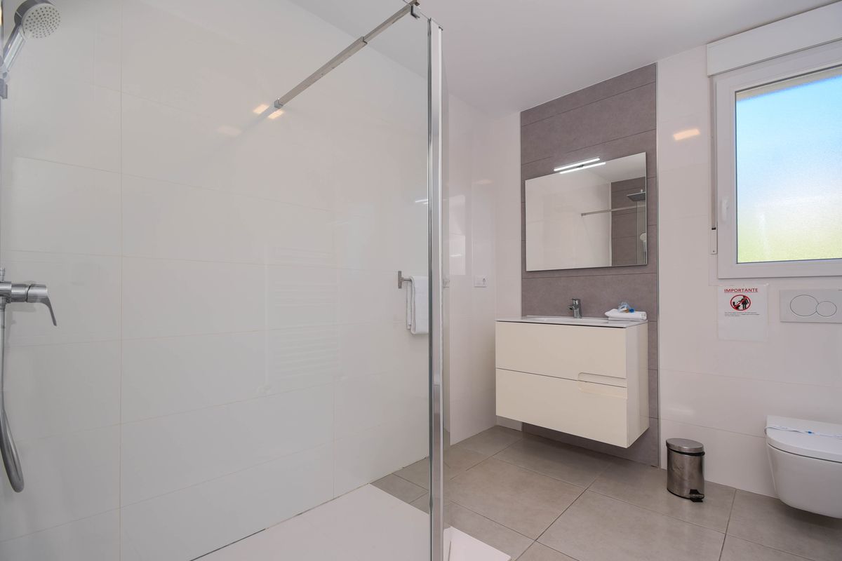 Salle de bain moderne avec douche à l'italienne vitrée, meuble vasque suspendu blanc sur mur gris et toilettes suspendues près d'une fenêtre dépolie.