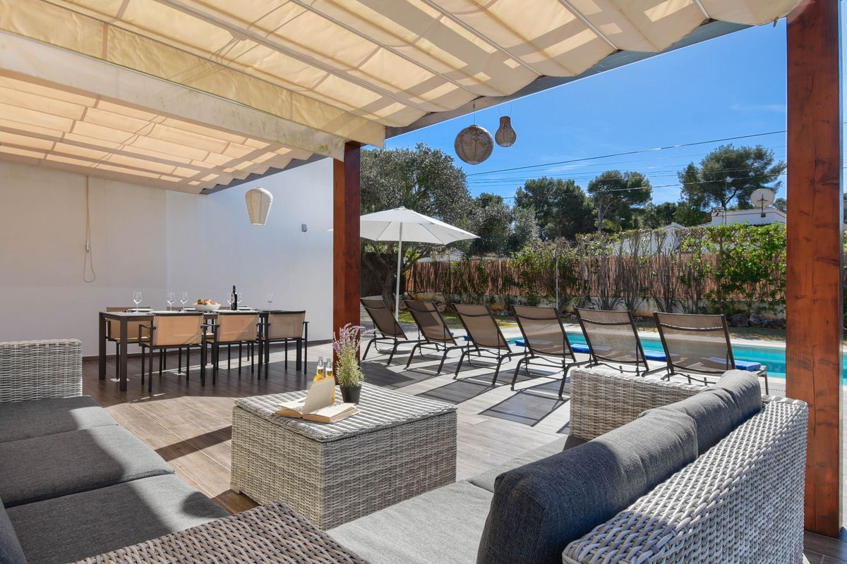 Terrasse avec auvent rétractable, salon de jardin en résine tressée, espace repas et chaises longues bordant une piscine privée.