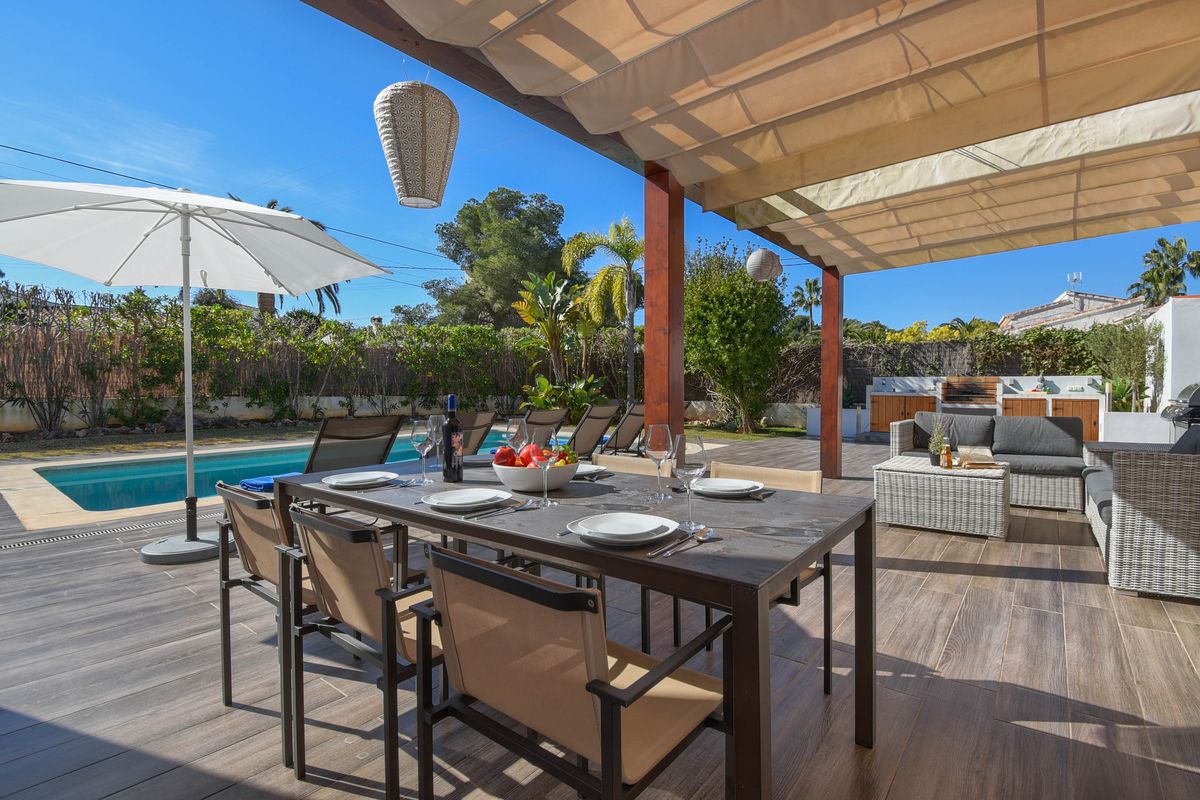 Terrasse extérieure avec espace repas sous auvent rétractable, sol en grès cérame aspect bois, piscine et salon de jardin avec cuisine d'été.
