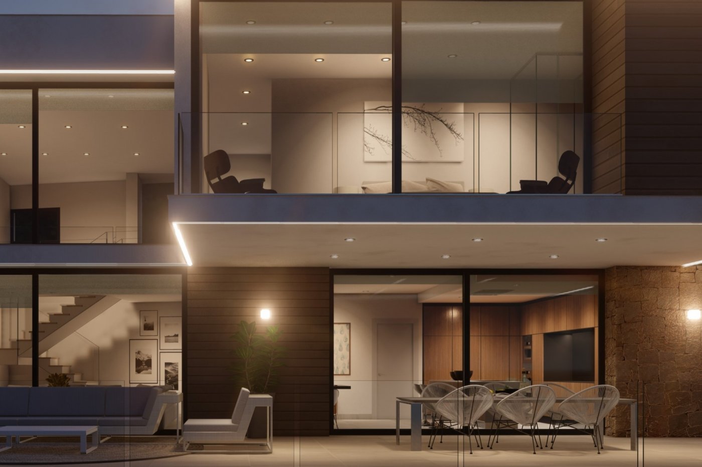 Vue nocturne d'une villa avec terrasse, chaises Acapulco et murs en pierre. Les baies vitrées révèlent une cuisine moderne et un balcon supérieur avec garde-corps en verre.