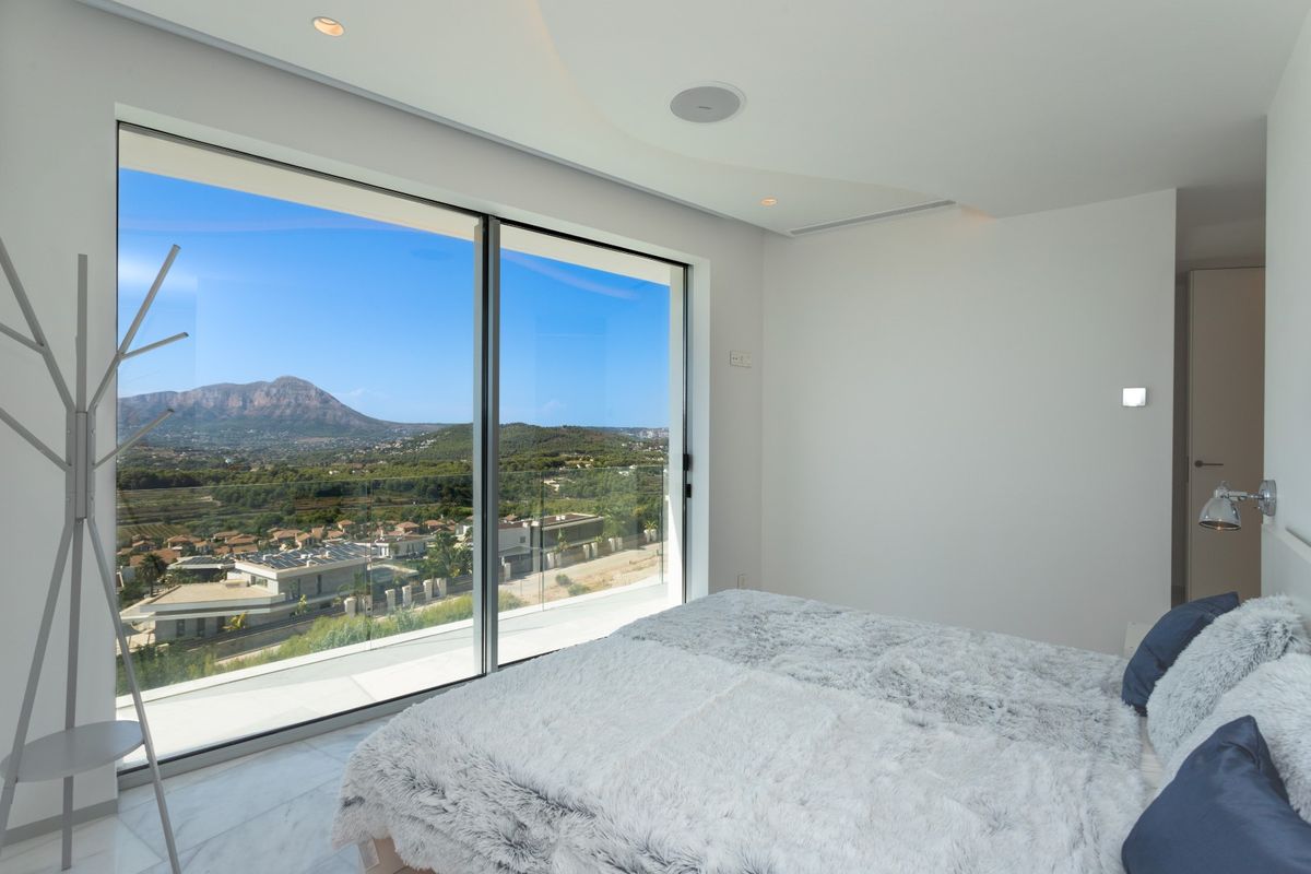 Chambre moderne avec de grandes baies vitrées offrant une vue sur le Montgó. Comprend un sol en marbre, des spots encastrés et des haut-parleurs intégrés au plafond.