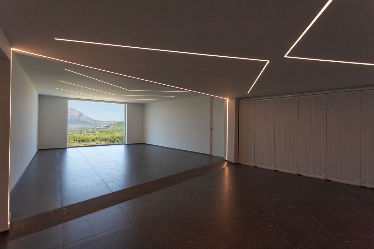 Espace minimaliste avec sol en grès cérame foncé et éclairage LED géométrique encastré. Une grande baie vitrée offre une vue sur la vallée et les montagnes.