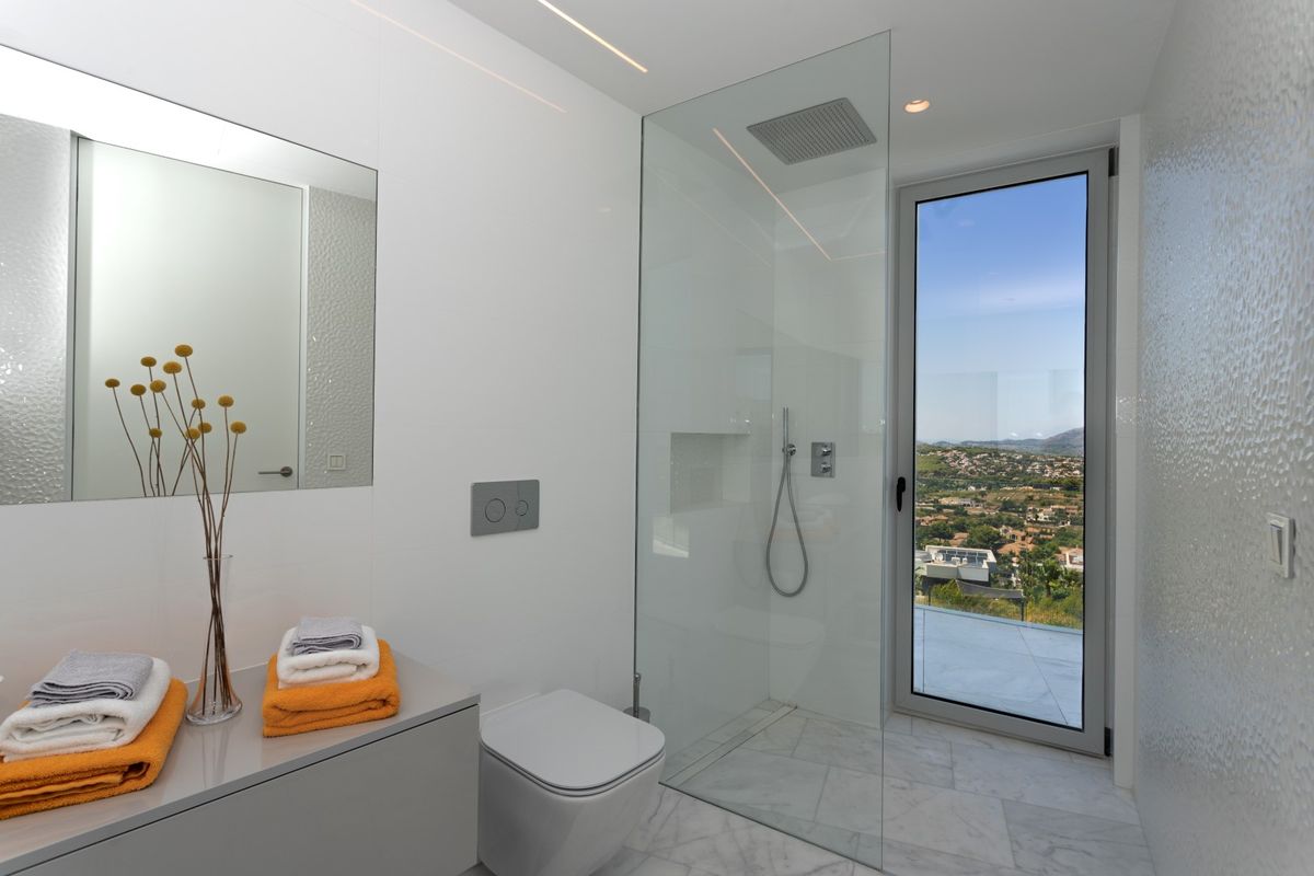 Salle de bain moderne avec douche à l'italienne vitrée, sol en marbre et accès direct à une terrasse offrant une vue dégagée sur la vallée.
