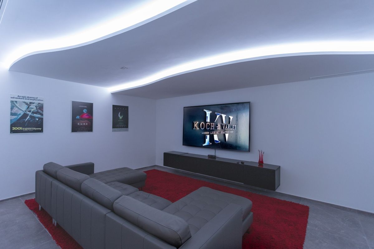Salle de cinéma privée dotée d'un plafond aux lignes ondulées avec éclairage LED, un canapé d'angle en cuir gris et une unité multimédia suspendue.