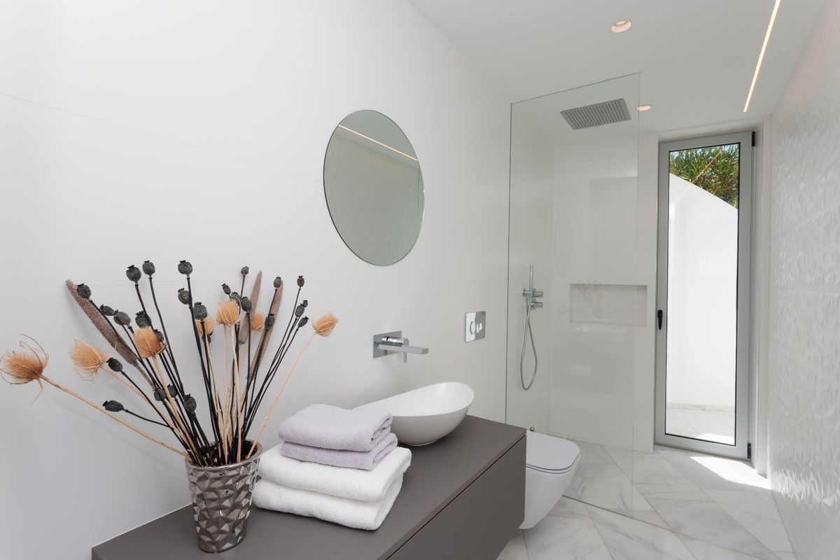 Salle d'eau contemporaine avec vasque à poser sur meuble suspendu gris, sol en marbre et douche à l'italienne vitrée ouvrant sur l'extérieur.