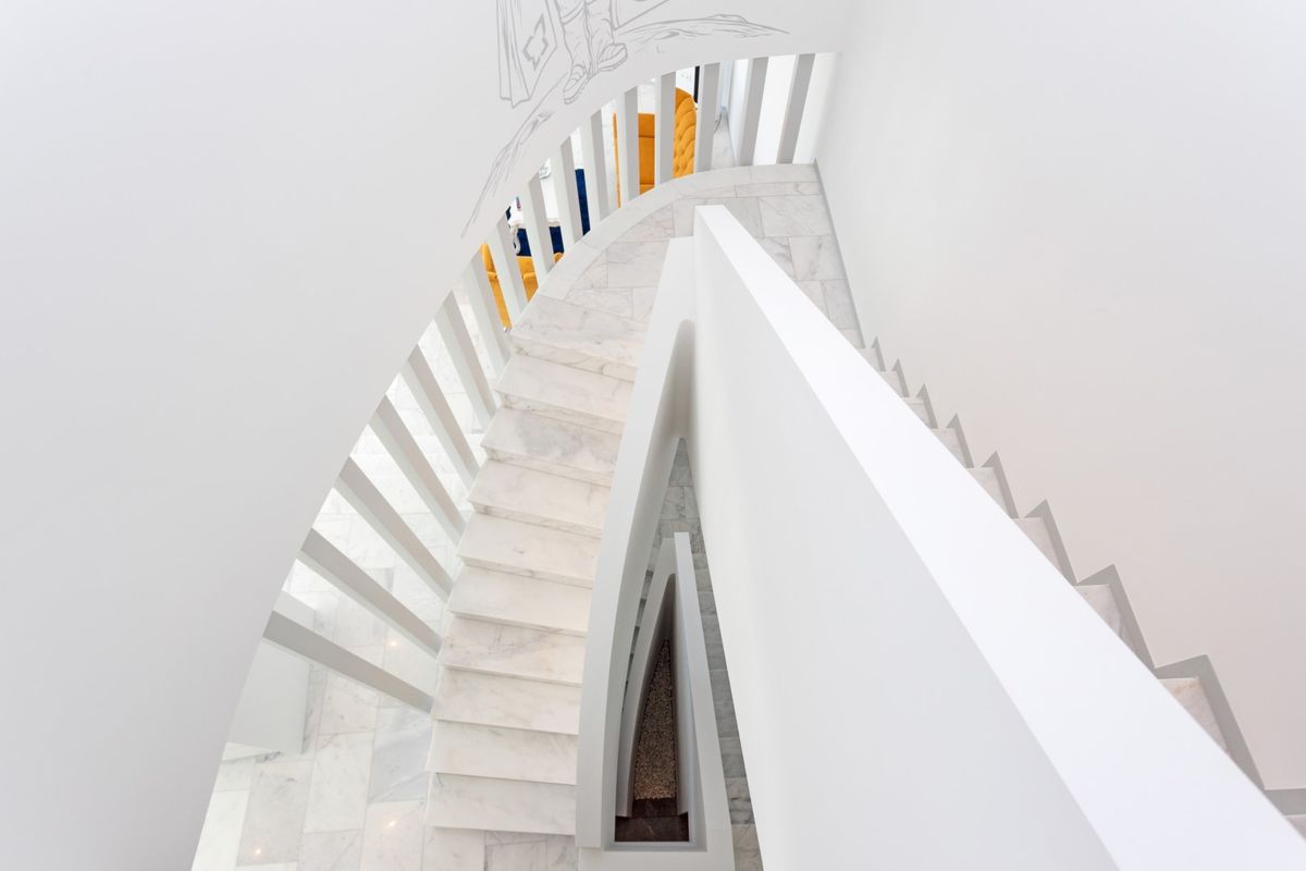 Vue plongeante d'un escalier tournant minimaliste avec des marches en marbre blanc et une balustrade à lattes verticales épurées.