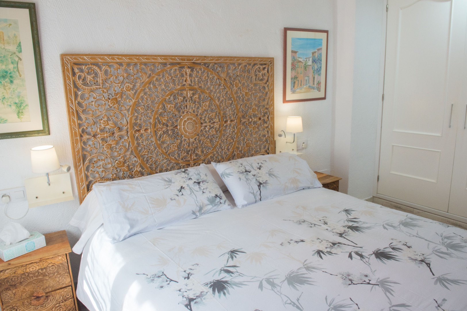 Chambre avec tête de lit en bois sculpté à la main, tables de chevet assorties et appliques murales à côté d'un placard intégré blanc.