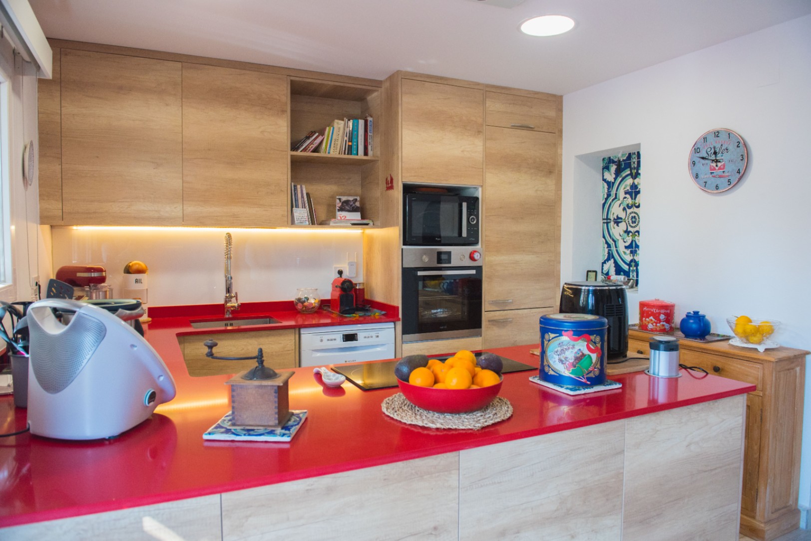 Cuisine moderne avec plan de travail rouge vif, meubles en bois clair et électroménagers encastrés, comprenant un four et une plaque à induction.