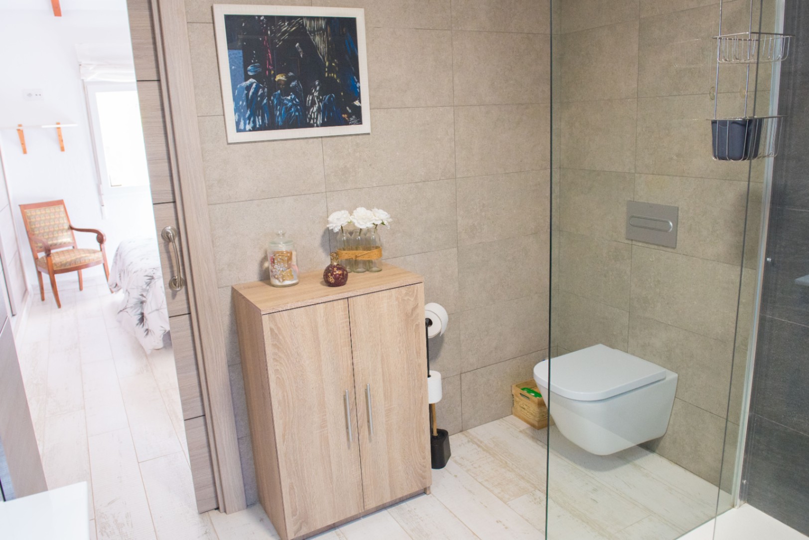 Salle d'eau moderne avec WC suspendu, paroi de douche en verre et meuble de rangement en bois clair sur carrelage aspect pierre.