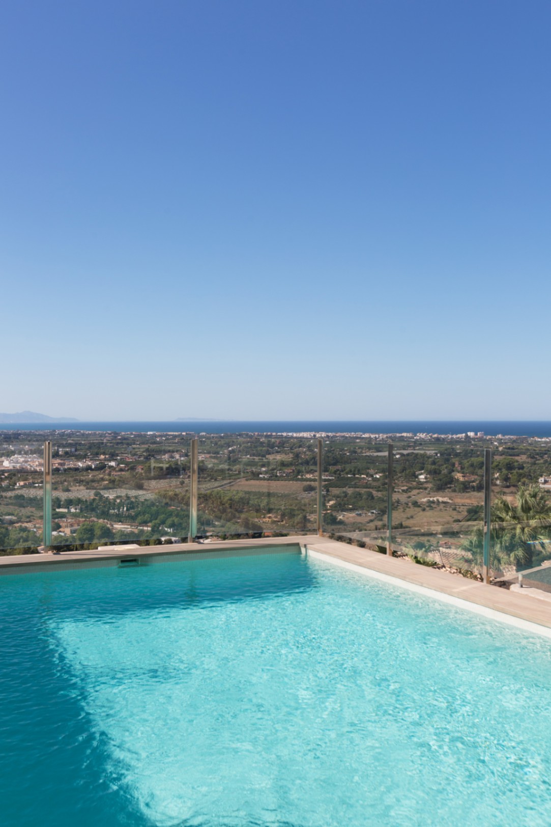 Piscine à débordement surélevée avec garde-corps en verre, offrant une vue panoramique sur la vallée côtière et la mer Méditerranée.