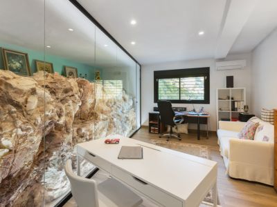 Bureau avec un mur de roche naturelle visible derrière une cloison vitrée, offrant un espace de travail distinctif. Il comprend deux bureaux et un canapé.