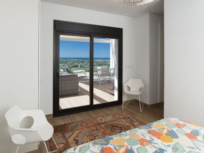 Chambre avec couette colorée, parquet et accès direct à une terrasse privée. De grandes portes coulissantes encadrent des vues panoramiques sur la mer et la côte, optimisant la lumière naturelle.