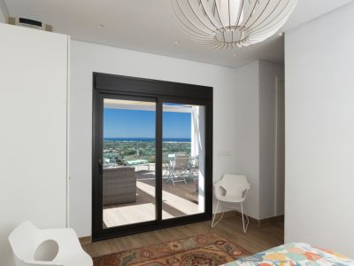 Chambre lumineuse avec accès direct à une terrasse privée offrant une vue panoramique. Elle est agrémentée d'un luminaire suspendu sphérique et de chaises modernes.