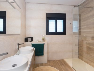 Salle de bain moderne avec double vasque ovale, robinetterie chromée et miroir éclairé. Douche à l'italienne avec paroi vitrée, carrelage mural effet bois et sol assorti.