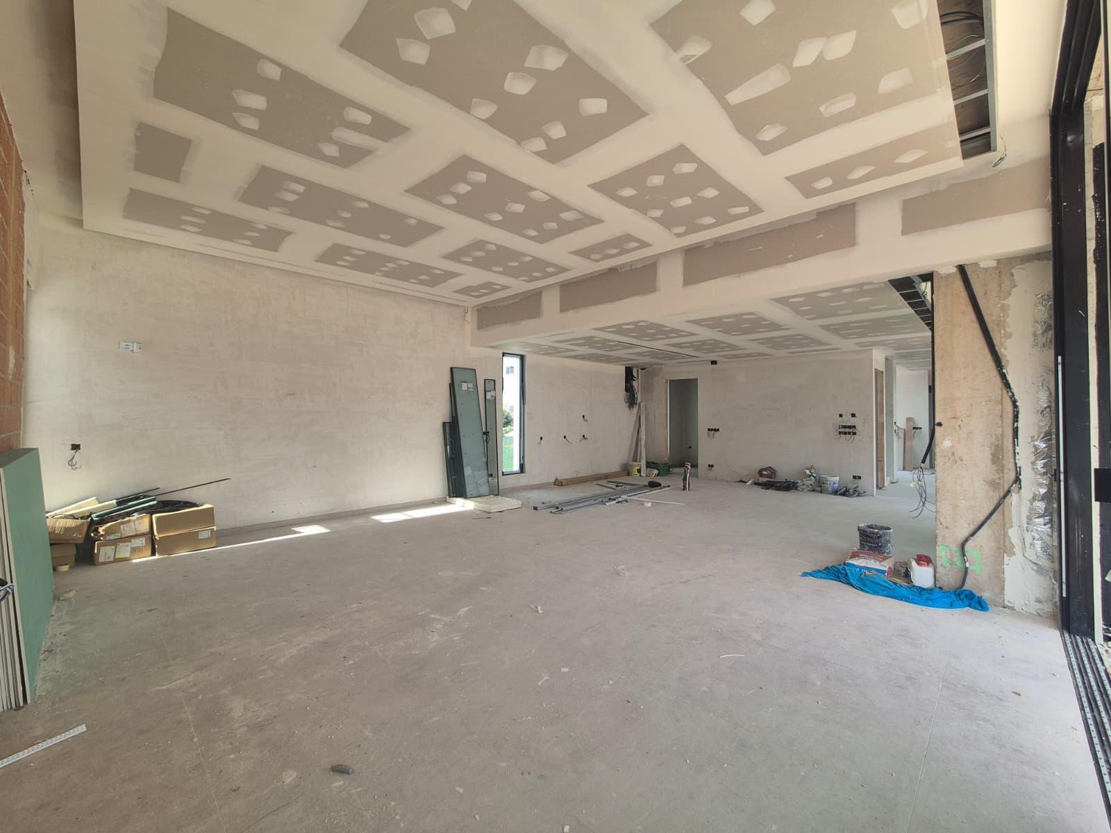 Vaste intérieur en cours de construction avec des plafonds en plaques de plâtre à plusieurs niveaux et de grandes ouvertures pour baies vitrées.