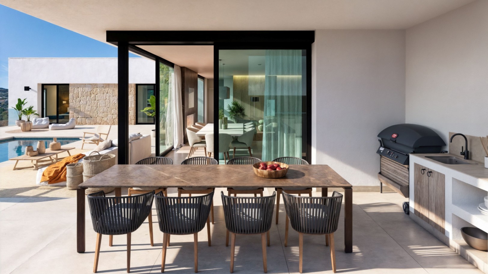 Terrasse couverte comprenant une grande table à manger en bois, des chaises en corde et une cuisine d'été avec barbecue et évier, offrant une vue sur la piscine.