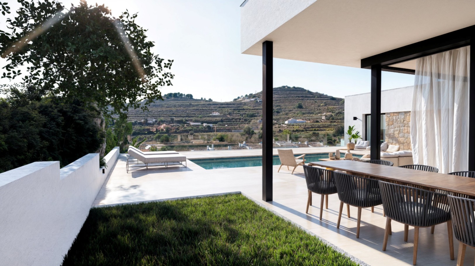 Terrasse extérieure moderne avec coin repas en bois, piscine et bains de soleil, surplombant un paysage de collines en terrasses et une vallée dégagée.
