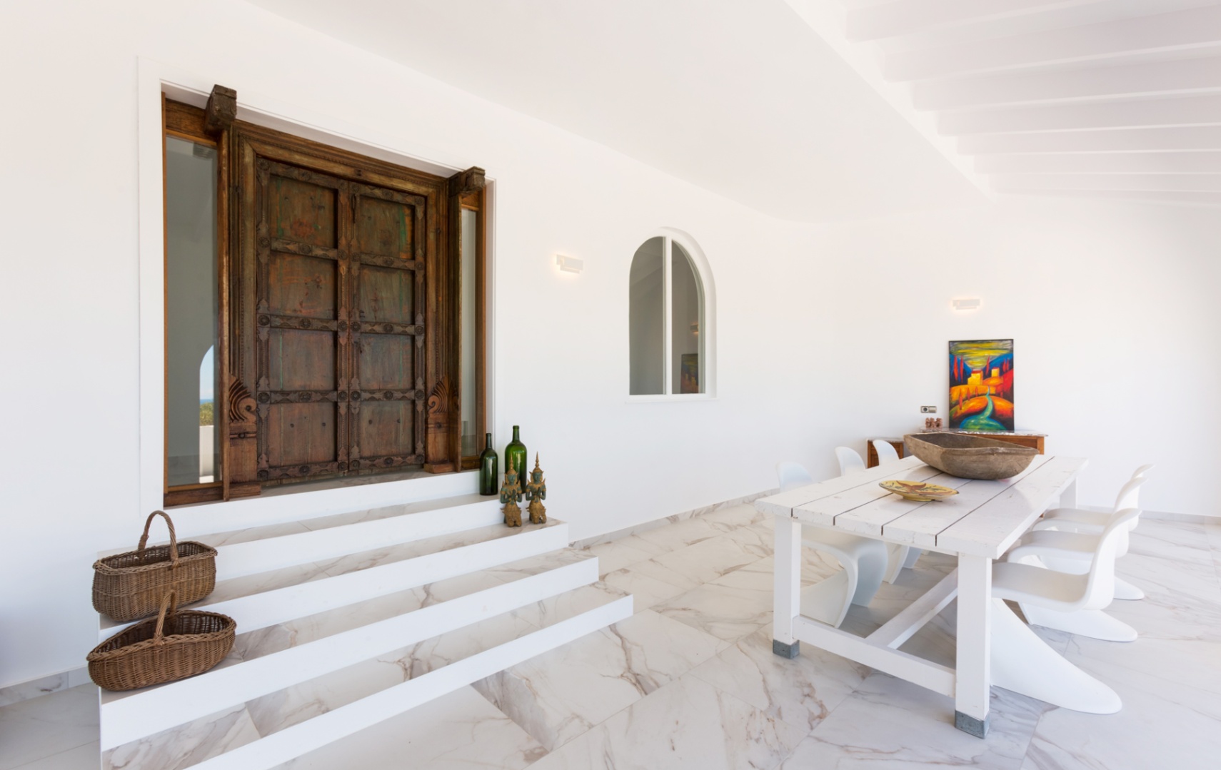 Entrée dotée d'une porte ancienne en bois sculpté, de marches en marbre blanc et d'un espace repas extérieur avec table rustique et chaises modernes.