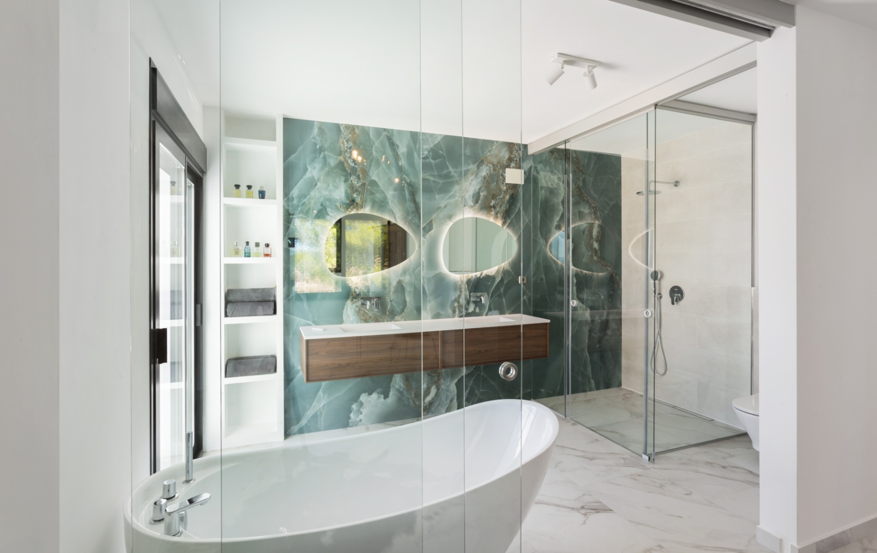 Salle de bain contemporaine avec mur en onyx vert, baignoire îlot et double vasque suspendue en bois. Miroirs rétroéclairés et douche à l'italienne avec parois en verre.