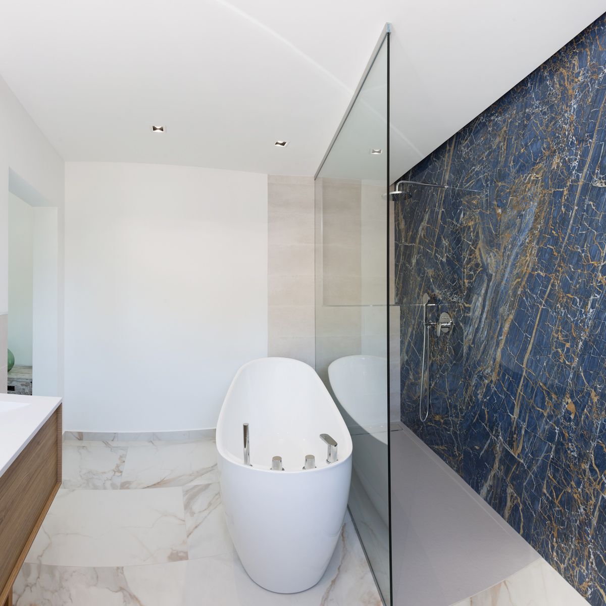 Salle de bain moderne avec baignoire îlot ovale, douche à l'italienne avec mur en marbre bleu et sol en marbre blanc aux veines dorées.