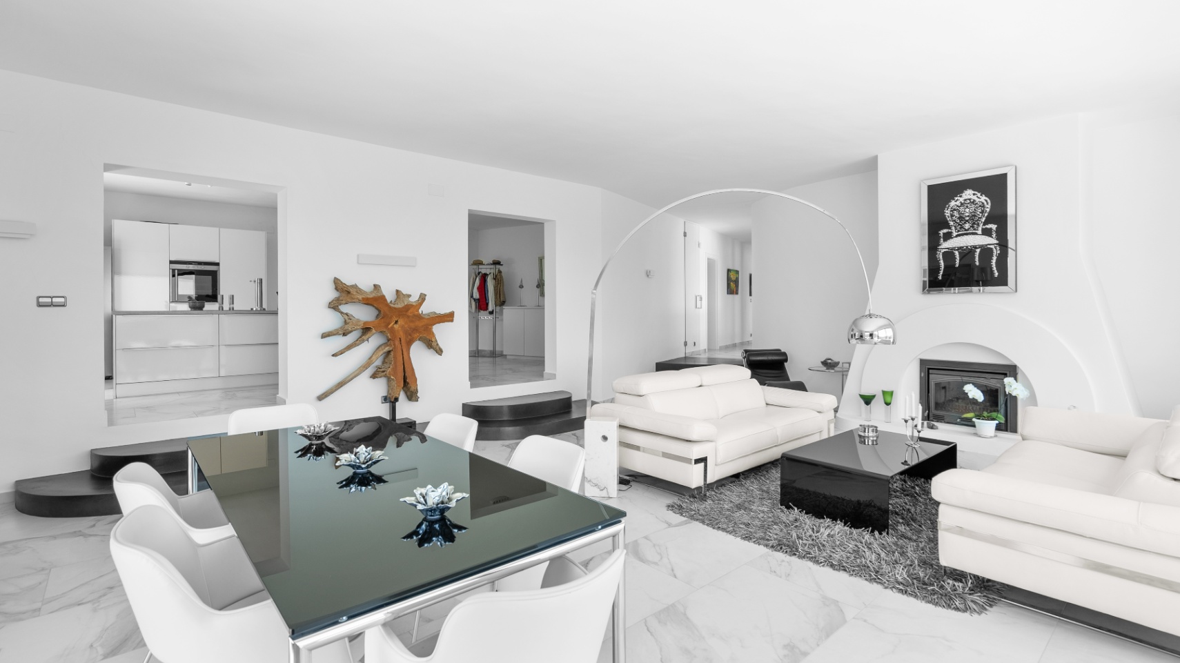 Salon et salle à manger à aire ouverte avec sol en marbre, canapés en cuir blanc, cheminée moderne et table en verre offrant une vue sur la cuisine.