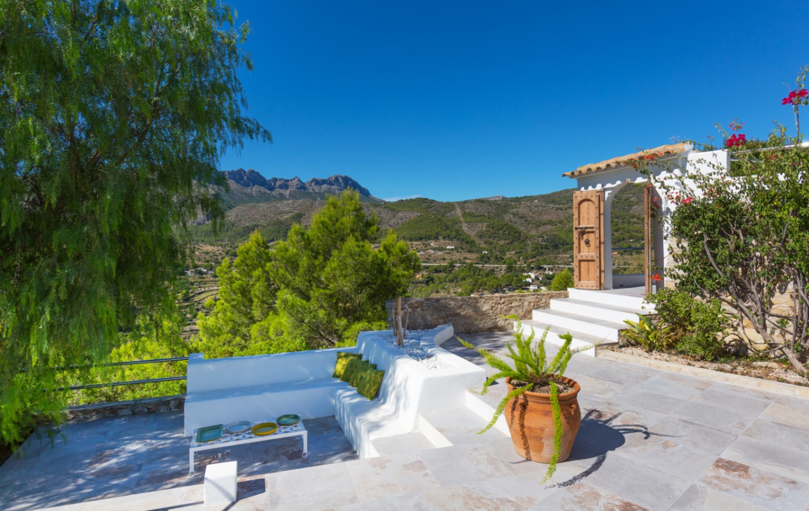 Terrasse avec banquettes en maçonnerie blanche, sol en pierre et vue panoramique sur les montagnes et la vallée.