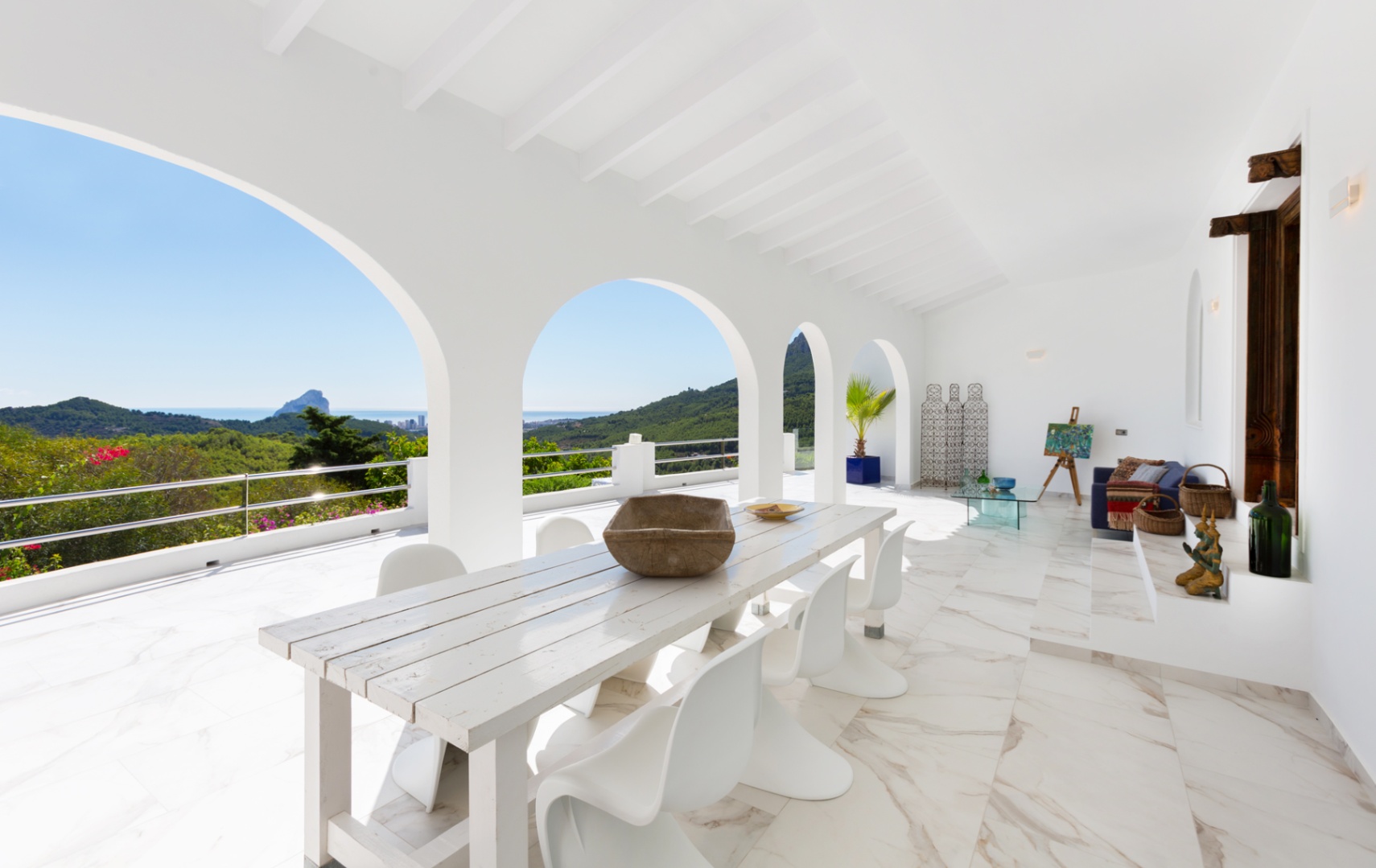 Terrasse couverte avec arches blanches, sol effet marbre et espace repas offrant une vue panoramique sur la côte méditerranéenne et le Peñón de Ifach.