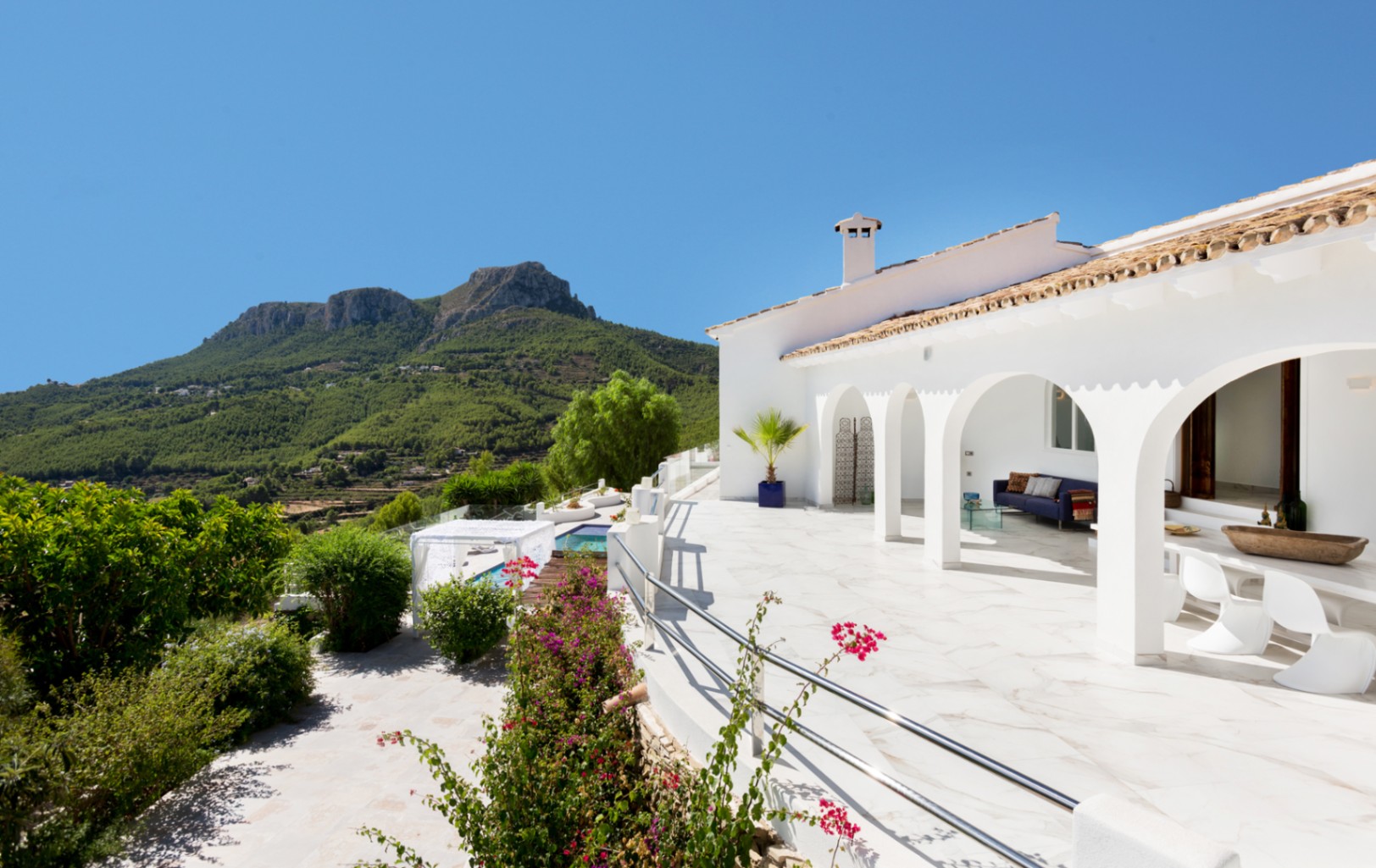 Villa méditerranéenne blanche dotée d'une terrasse à arcades avec sol en marbre, d'un salon extérieur et d'une vue dégagée sur les montagnes.
