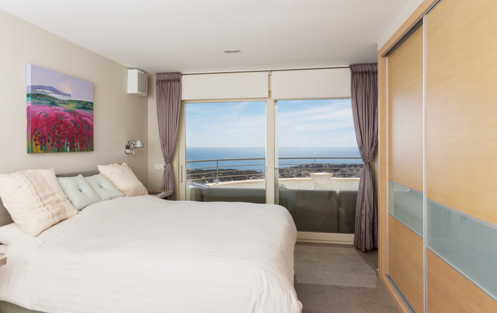 Chambre moderne avec placard intégré en bois et grandes baies vitrées ouvrant sur une terrasse offrant une vue panoramique sur la mer.
