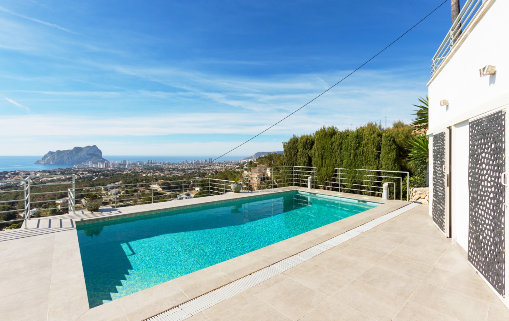 Piscine extérieure rectangulaire avec terrasse en carrelage et garde-corps métallique, offrant une vue panoramique sur la mer Méditerranée et le Peñón de Ifach.