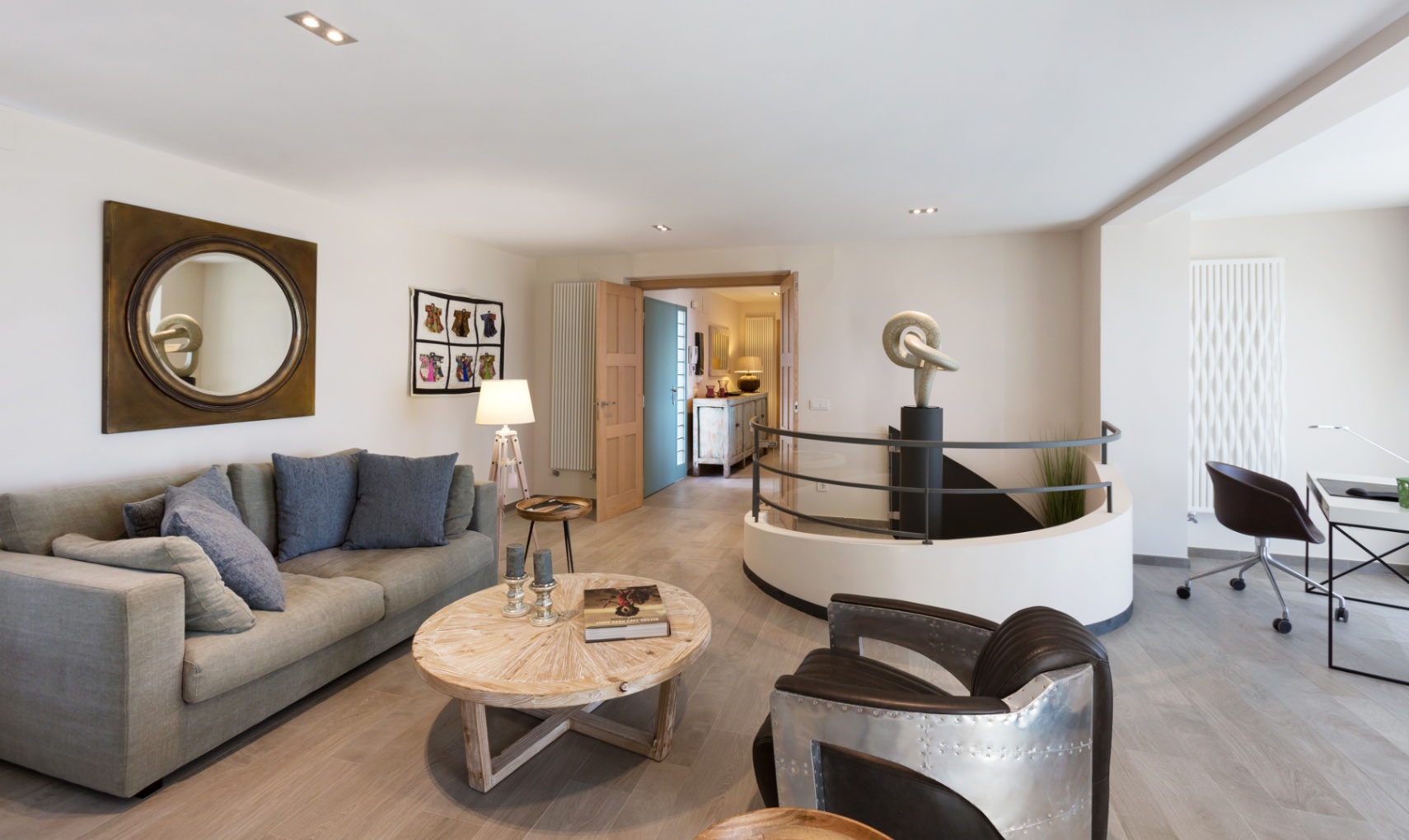 Salon moderne avec canapé gris, fauteuil style aviateur et escalier circulaire orné d'une sculpture. Comprend un espace bureau et un parquet en bois clair.