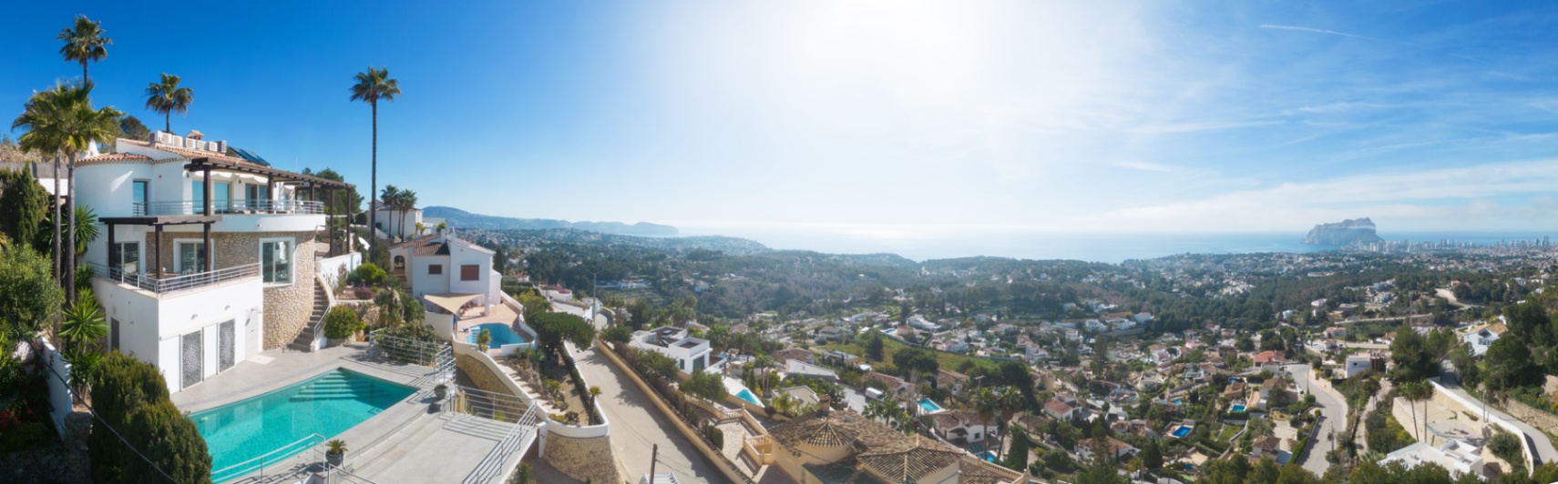 Vue panoramique d'une villa méditerranéenne avec piscine privée, façades en pierre et terrasses spacieuses offrant une vue sur le littoral et le Peñón de Ifach.