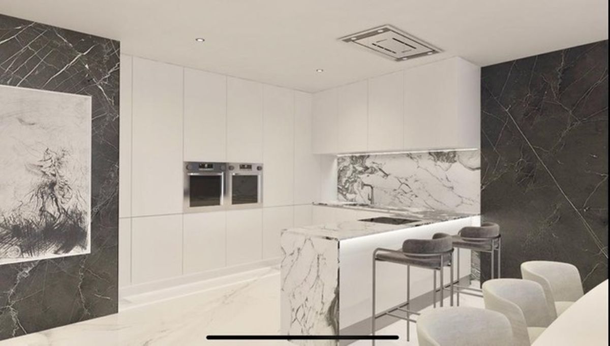 Cuisine moderne avec placards blancs minimalistes, îlot en marbre veiné, fours doubles intégrés et panneaux muraux en marbre sombre avec éclairage encastré.