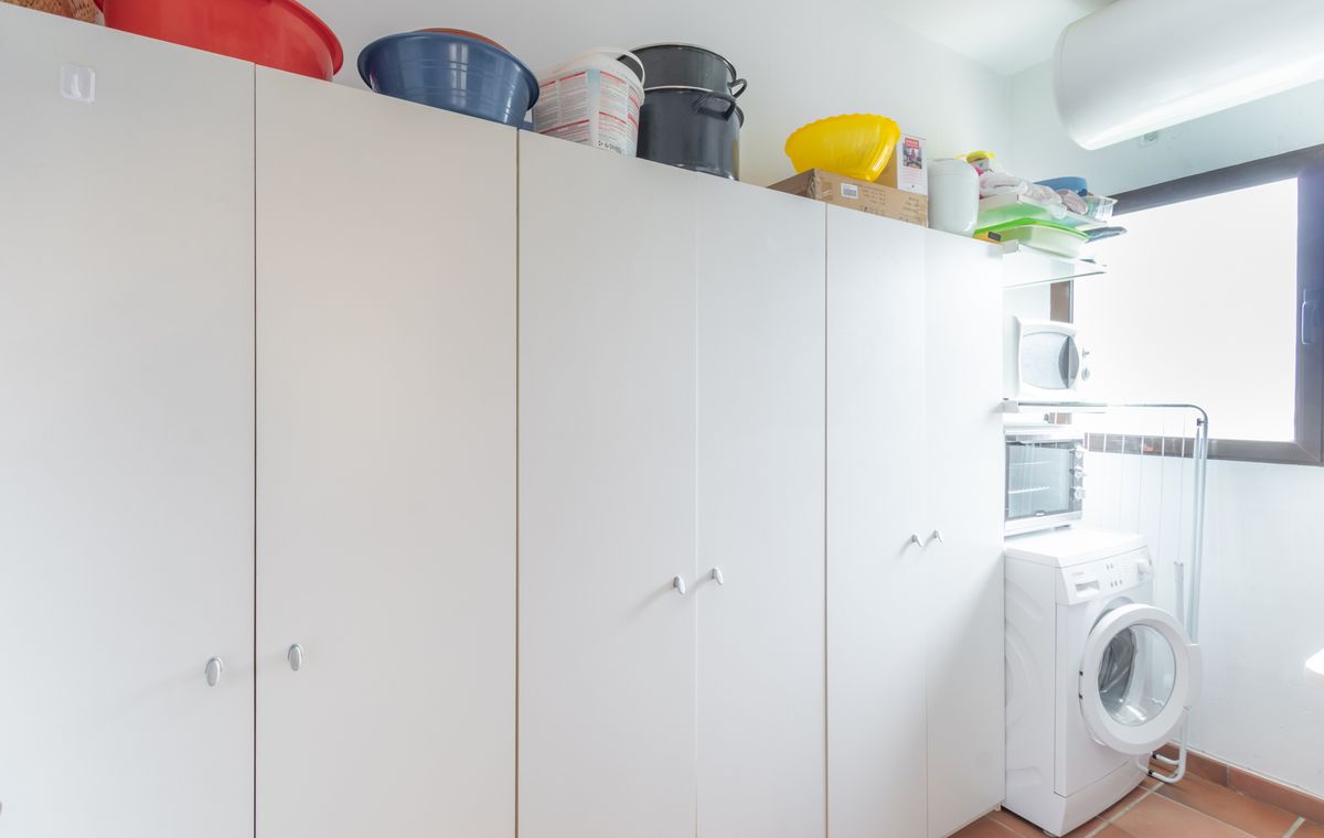 Buanderie avec de grands placards de rangement blancs, un sol en terre cuite et un espace dédié au lave-linge et aux petits appareils.