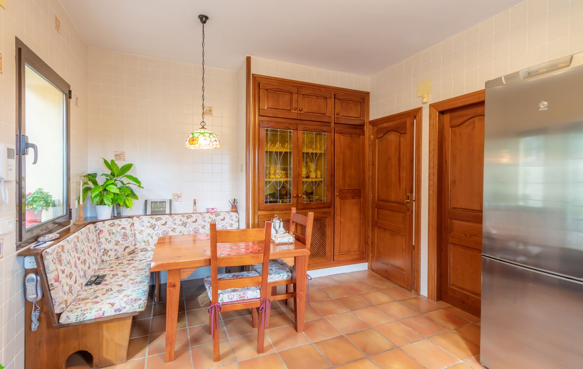 Coin repas de cuisine avec banquette en bois intégrée, carrelage en terre cuite et placards en bois massif avec vitrines.