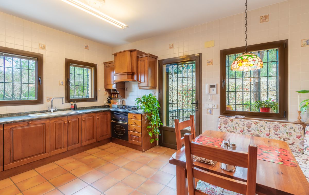 Cuisine rustique avec meubles en bois, sol en terre cuite et coin repas doté d'une suspension style Tiffany et d'une banquette aux motifs floraux.