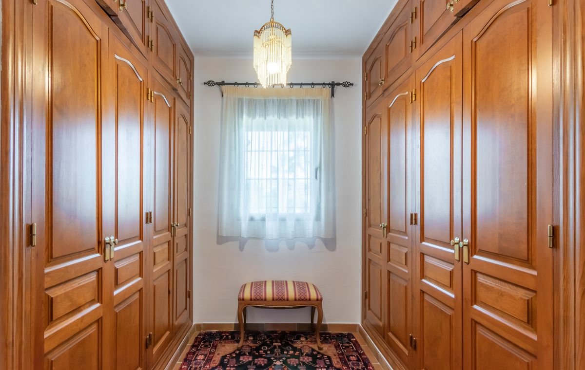 Dressing avec armoires encastrées en bois massif, lustre classique et fenêtre centrale apportant une lumière naturelle.