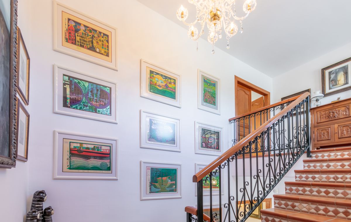 Escalier avec marches en terre cuite, rampe en fer forgé et mur de galerie orné d'œuvres d'art encadrées, éclairé par un lustre en cristal élégant.