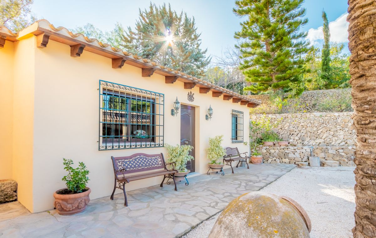 Façade méditerranéenne avec poutres en bois apparentes, fenêtres à grilles en fer forgé et terrasse en pierre naturelle avec bancs ornementaux.