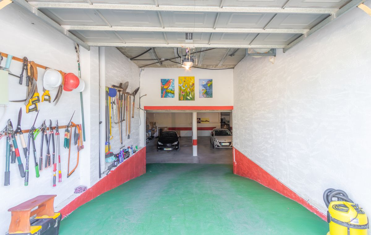 Garage spacieux comprenant une rampe d'accès verte, un mur d'outils organisé et un espace de stationnement inférieur pour plusieurs voitures.