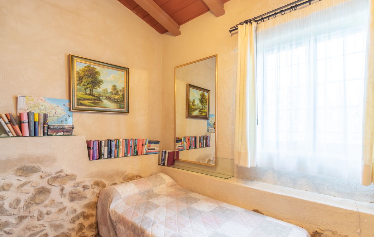 Petite chambre avec lit simple, poutres apparentes en bois et mur en pierre rustique. Équipée d'étagères en verre intégrées et d'un grand miroir vertical.