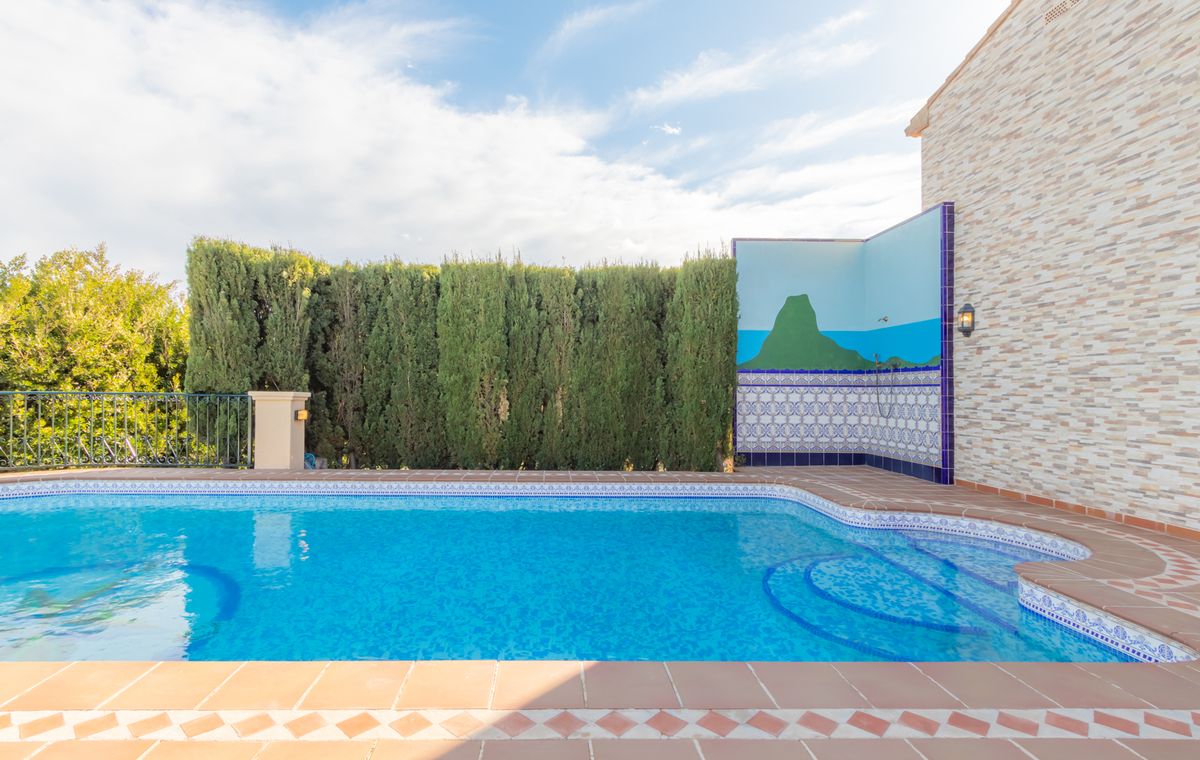 Piscine extérieure avec marches d'accès courbées, terrasse en terre cuite et douche d'été ornée d'une fresque et de carreaux décoratifs.